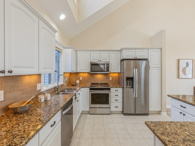 kitchen featuring high vaulted ceiling, white cabinets, sink, dark stone countertops, and stainless steel appliances