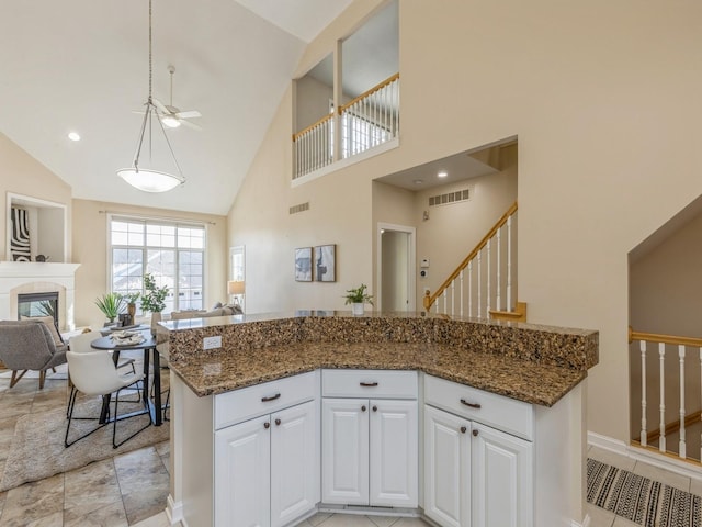 kitchen with white cabinetry, ceiling fan, dark stone countertops, a towering ceiling, and decorative light fixtures