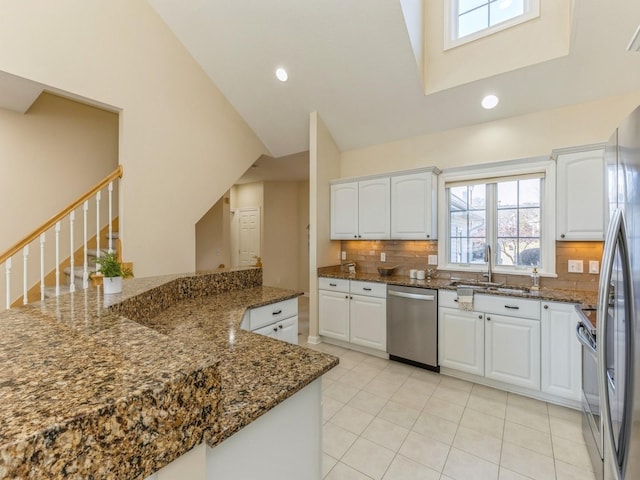 kitchen with white cabinets, backsplash, stainless steel appliances, and dark stone countertops