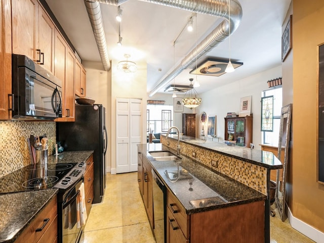 kitchen with a large island with sink, hanging light fixtures, sink, dark stone countertops, and stainless steel appliances