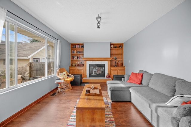 living room featuring built in shelves, a tile fireplace, and hardwood / wood-style flooring