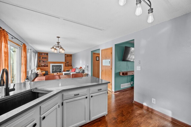 kitchen featuring dark wood-type flooring, sink, white cabinetry, decorative light fixtures, and built in features