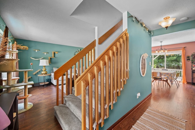 stairway featuring wood-type flooring, an inviting chandelier, and a textured ceiling