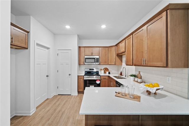 kitchen with sink, light stone counters, kitchen peninsula, light hardwood / wood-style floors, and appliances with stainless steel finishes