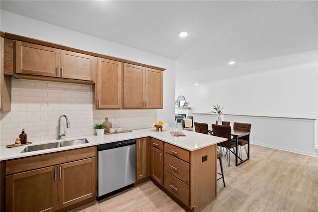 kitchen with dishwasher, sink, light hardwood / wood-style floors, kitchen peninsula, and a breakfast bar area