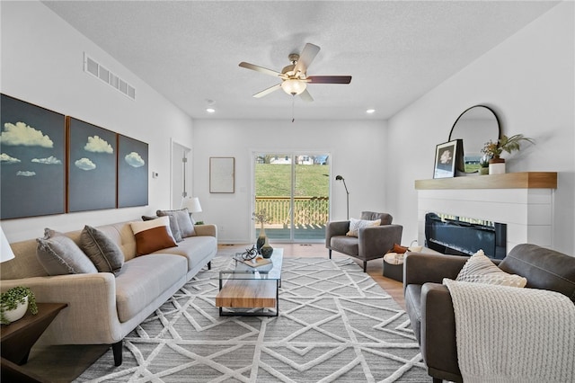 living room with a textured ceiling, light hardwood / wood-style flooring, and ceiling fan