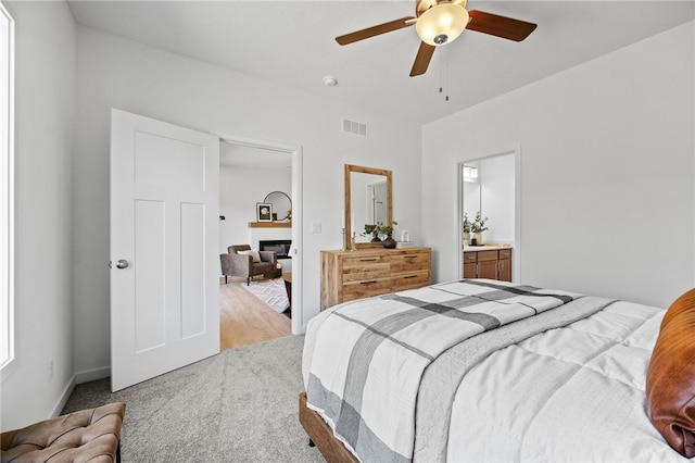 bedroom with ceiling fan, ensuite bathroom, and light carpet