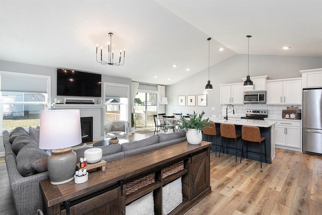 living room featuring light hardwood / wood-style floors, lofted ceiling, sink, and an inviting chandelier