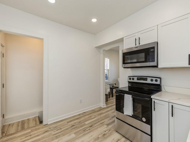 kitchen with light stone counters, stainless steel appliances, white cabinets, and light wood-type flooring