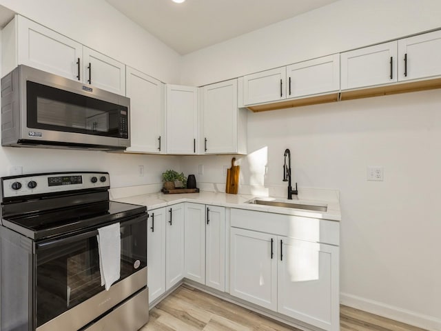 kitchen with sink, white cabinets, stainless steel appliances, light stone countertops, and light hardwood / wood-style flooring