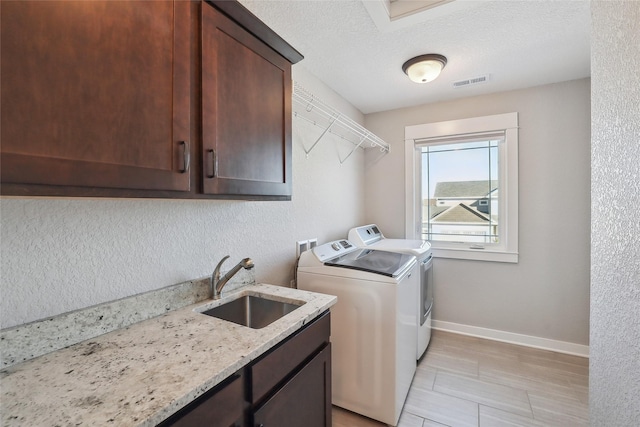 washroom with cabinet space, visible vents, washing machine and dryer, a sink, and baseboards