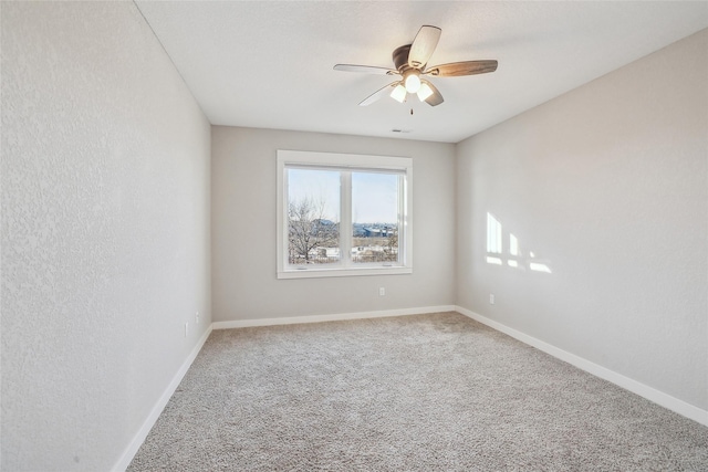 carpeted empty room with ceiling fan, a textured wall, and baseboards