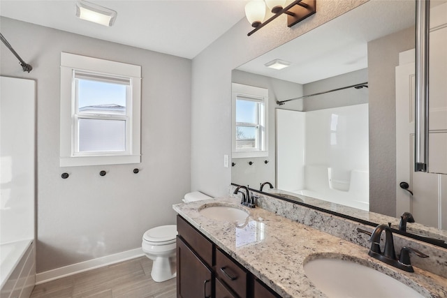 full bath featuring double vanity, a sink, toilet, and baseboards