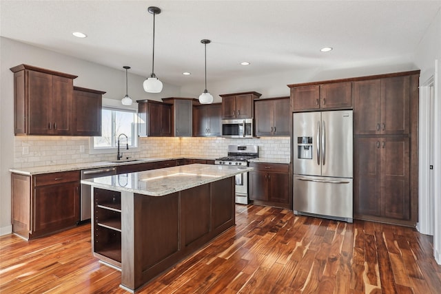 kitchen featuring a kitchen island, appliances with stainless steel finishes, light stone counters, decorative light fixtures, and a sink