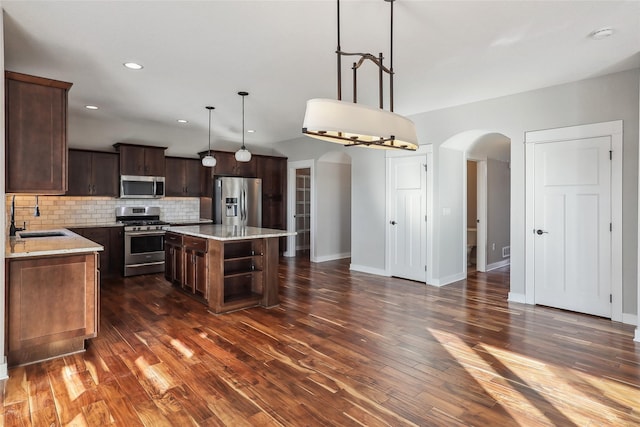 kitchen featuring arched walkways, stainless steel appliances, a sink, a center island, and pendant lighting