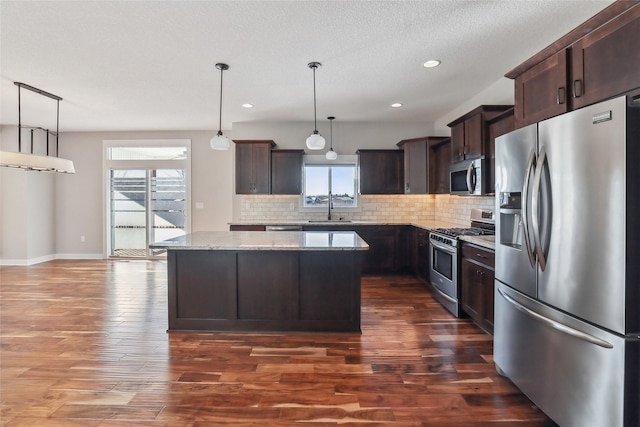 kitchen with light stone counters, stainless steel appliances, a sink, a kitchen island, and pendant lighting