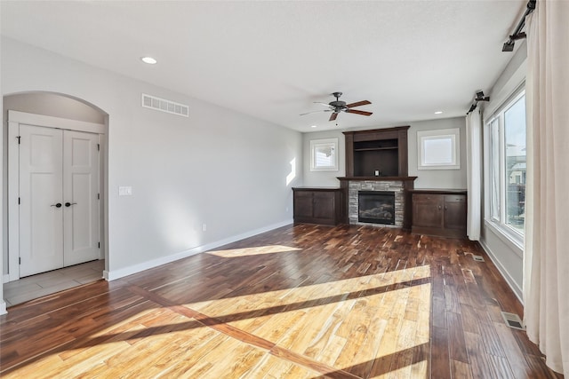 unfurnished living room with dark wood-style floors, visible vents, a wealth of natural light, and a stone fireplace