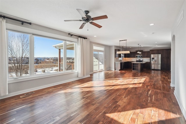 unfurnished living room with baseboards, visible vents, arched walkways, and dark wood finished floors