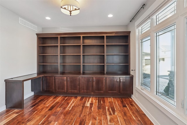 unfurnished office with a healthy amount of sunlight, visible vents, baseboards, and dark wood-style flooring