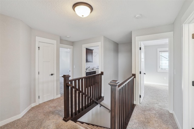 hall featuring carpet, baseboards, a textured ceiling, and an upstairs landing