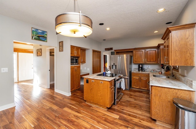 kitchen with sink, dark wood-type flooring, stainless steel appliances, decorative light fixtures, and a kitchen island