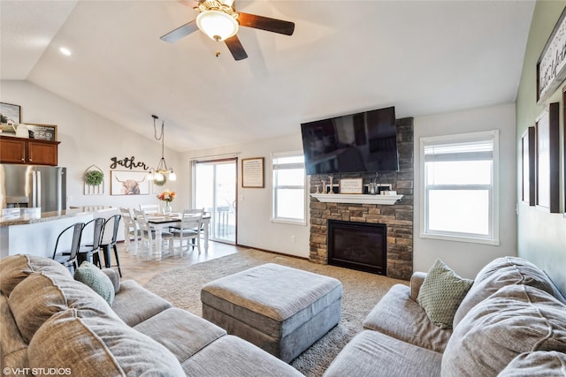 living room with ceiling fan with notable chandelier, a healthy amount of sunlight, a stone fireplace, and lofted ceiling