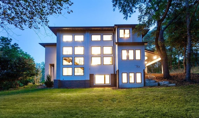 back house at dusk featuring a lawn