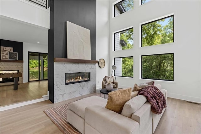 living room featuring a tiled fireplace, a towering ceiling, and light wood-type flooring