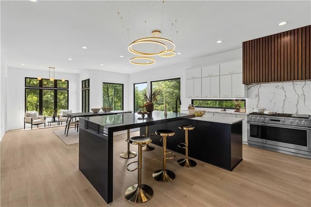 kitchen with a breakfast bar area, decorative light fixtures, a center island, high end stove, and white cabinets