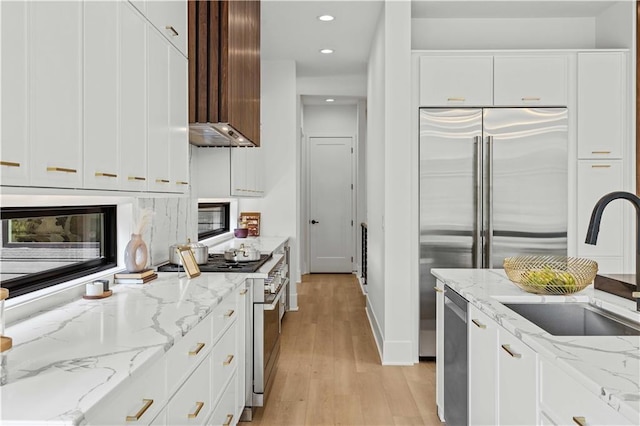 kitchen featuring white cabinetry, sink, premium appliances, light stone counters, and light hardwood / wood-style floors