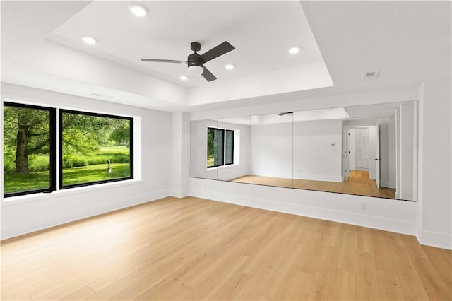 unfurnished living room featuring light hardwood / wood-style flooring, ceiling fan, and a tray ceiling