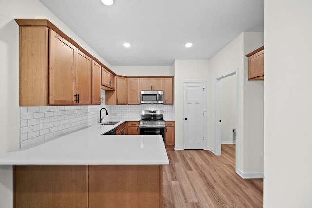 kitchen featuring kitchen peninsula, light wood-type flooring, backsplash, stainless steel appliances, and sink