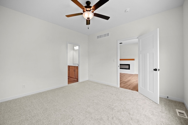 unfurnished bedroom with ensuite bath, ceiling fan, and light carpet