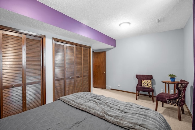 bedroom with a textured ceiling, light carpet, and multiple closets