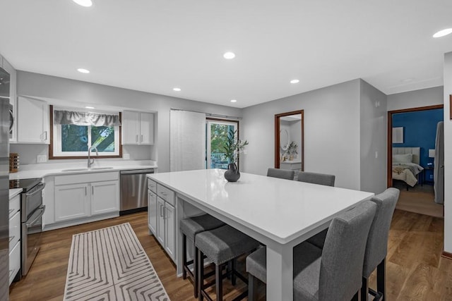 kitchen with stainless steel appliances, dark wood-type flooring, sink, white cabinets, and a kitchen island