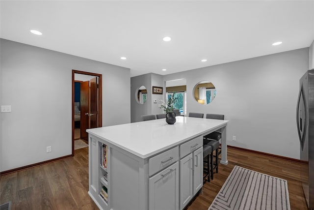 kitchen featuring stainless steel fridge, dark hardwood / wood-style flooring, a kitchen breakfast bar, a center island, and gray cabinets