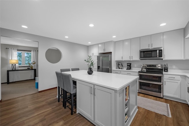 kitchen with appliances with stainless steel finishes, a center island, white cabinetry, and dark hardwood / wood-style flooring