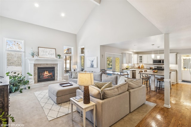 living room with a tile fireplace, sink, high vaulted ceiling, beamed ceiling, and light wood-type flooring