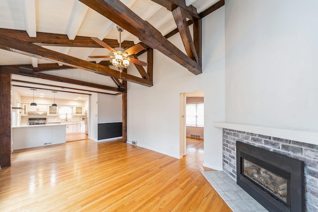 unfurnished living room with ceiling fan, a brick fireplace, beamed ceiling, high vaulted ceiling, and light hardwood / wood-style floors