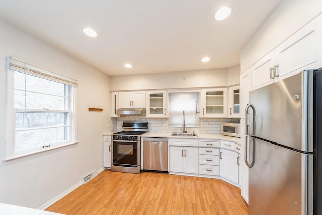 kitchen featuring white cabinetry, sink, backsplash, appliances with stainless steel finishes, and light wood-type flooring