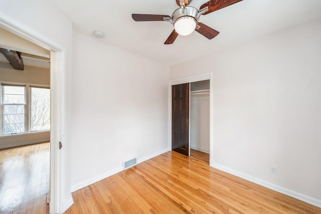 unfurnished bedroom featuring beamed ceiling, wood-type flooring, a closet, and ceiling fan