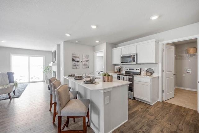 kitchen featuring light countertops, appliances with stainless steel finishes, dark wood-type flooring, and a breakfast bar area