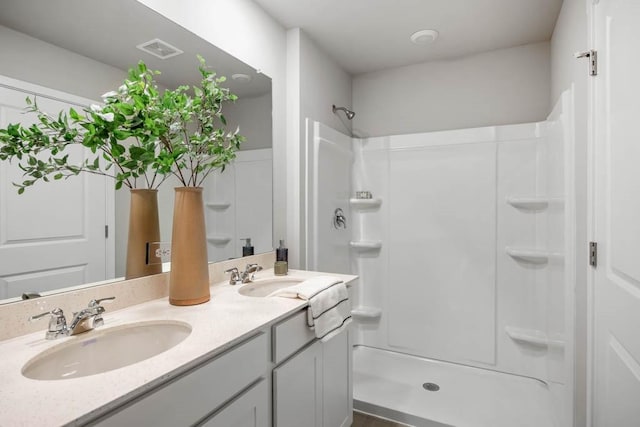 bathroom with a shower, double vanity, a sink, and visible vents