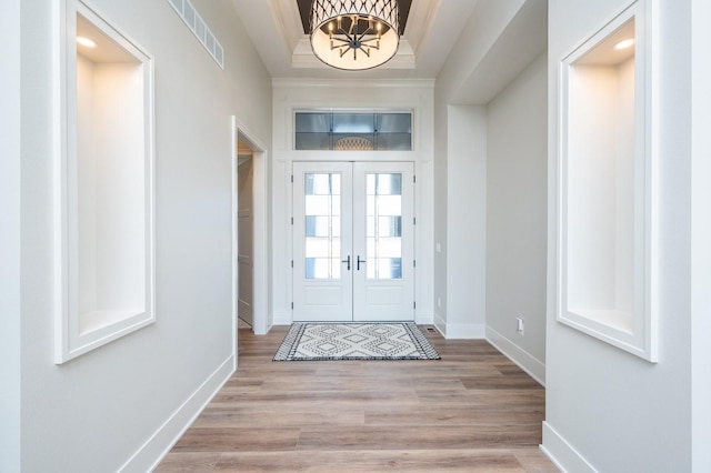 doorway featuring crown molding, french doors, light wood-type flooring, and a notable chandelier