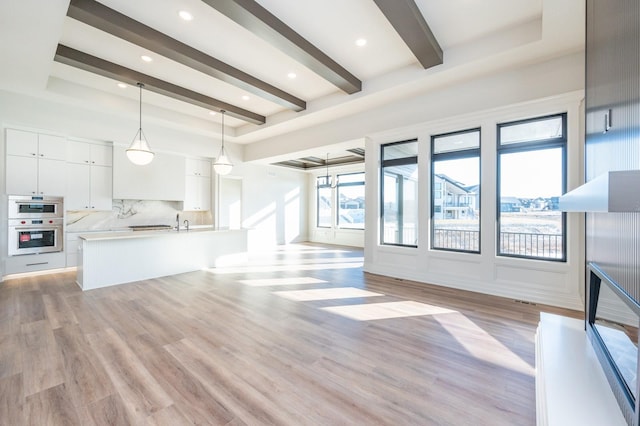 unfurnished living room with beamed ceiling, light wood-type flooring, and sink