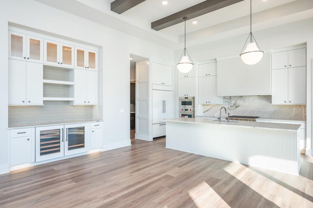 kitchen featuring white cabinets, light wood-type flooring, decorative light fixtures, and a kitchen island with sink