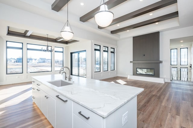 kitchen featuring sink, a fireplace, an island with sink, decorative light fixtures, and white cabinetry