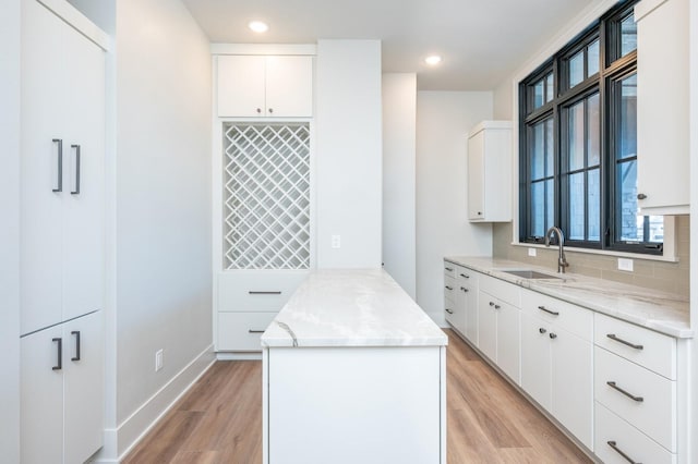 kitchen with white cabinets, light hardwood / wood-style floors, light stone countertops, and sink