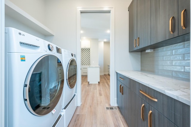 clothes washing area featuring washer and clothes dryer, cabinets, and light hardwood / wood-style flooring