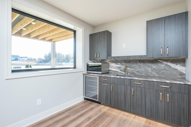 kitchen featuring decorative backsplash, sink, stone counters, light hardwood / wood-style floors, and wine cooler